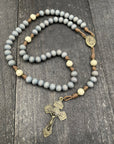 Lightweight rosary with smooth beads, featuring a detailed metallic pendant and crucifix, elegantly displayed on a gray table, ideal for daily use or as a meaningful gift.