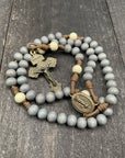 Rosary with gray beads, a metal crucifix, and a religious medal on a wooden surface.