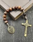 Full view of a rosary with sand-colored beads, durable knots, a detailed copper-colored crucifix, and a beautiful pendant, lying on a book placed on a light wooden table, ideal for prayer and spiritual reflection.