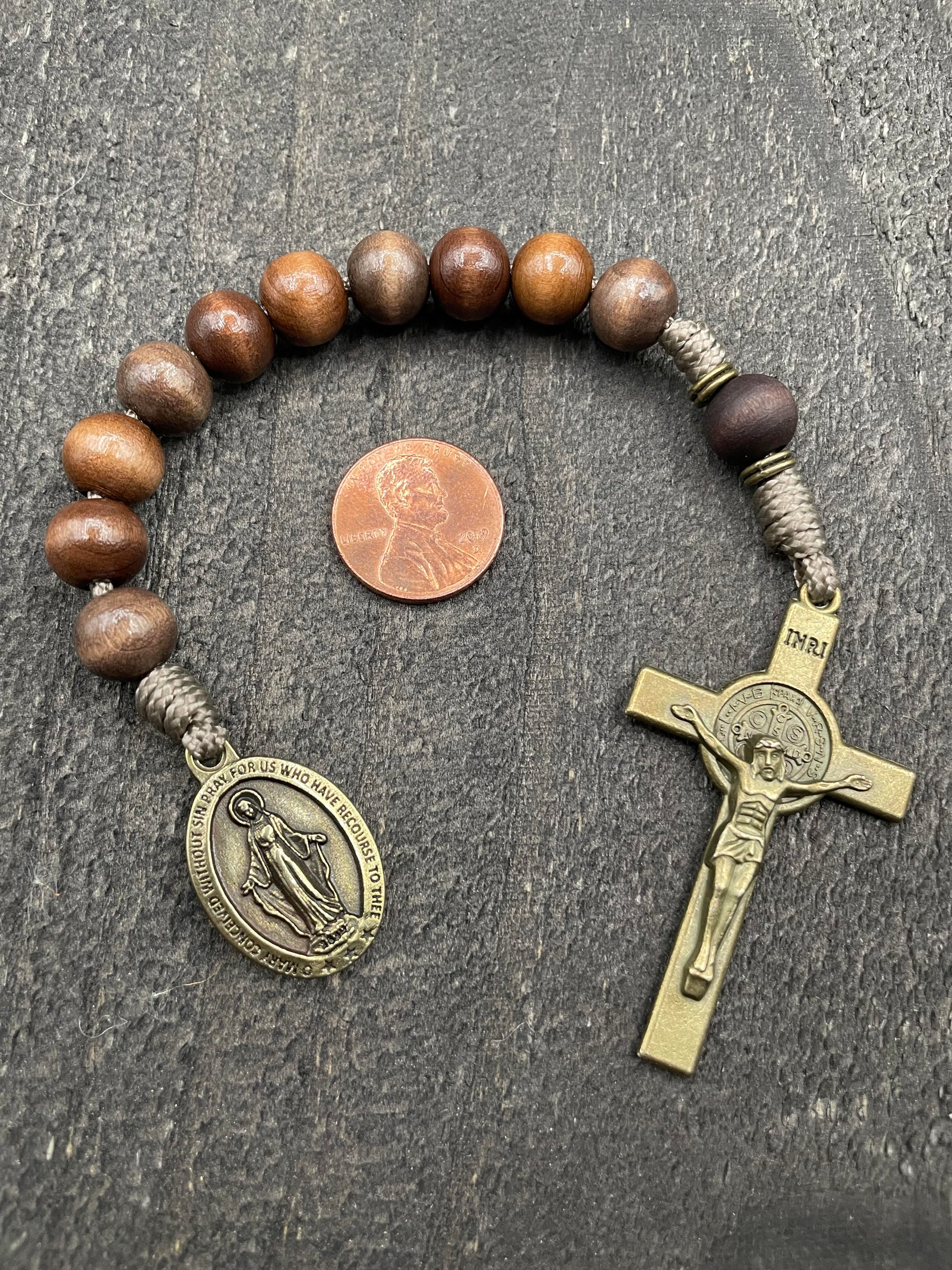 Close-up of a rosary with sand-colored beads, durable knots, a detailed copper-colored crucifix, and a beautiful pendant, displayed on a light wooden surface with a penny for size comparison, ideal for prayer and reflection.