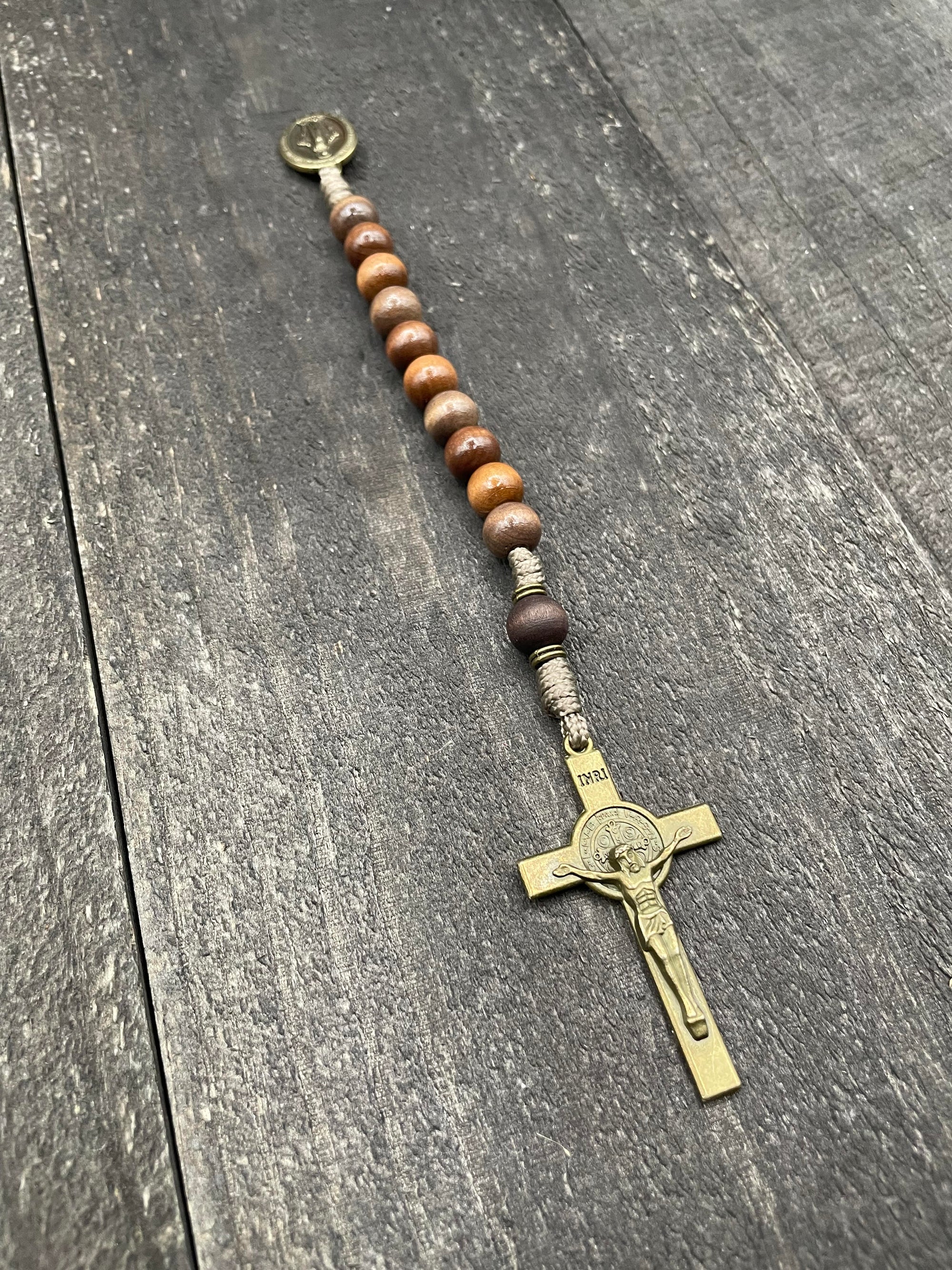 Close-up of a rosary with sand-colored beads, durable knots, and a detailed silver crucifix, displayed on a light wooden surface, ideal for prayer and meditation.