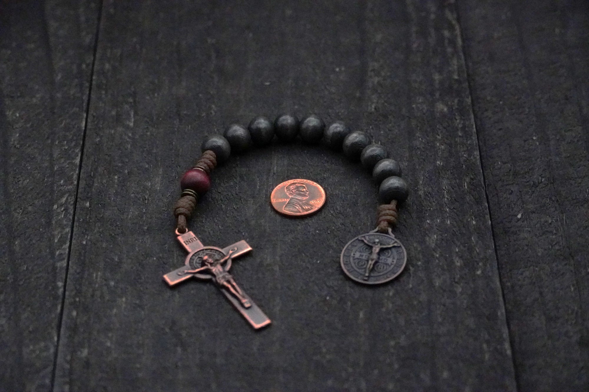 Handmade paracord rosary featuring charcoal wood beads and bronze Pardon Crucifix hardware