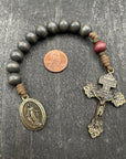 Full view of a rosary with dark wooden beads, durable knots, a detailed golden metallic crucifix, and a beautiful pendant, displayed on a light wooden surface with a penny for size comparison, ideal for prayer and reflection.