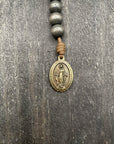 Close-up of a detailed rosary pendant with dark wooden beads and durable knots, placed on a light wooden table, ideal for prayer and reflection.