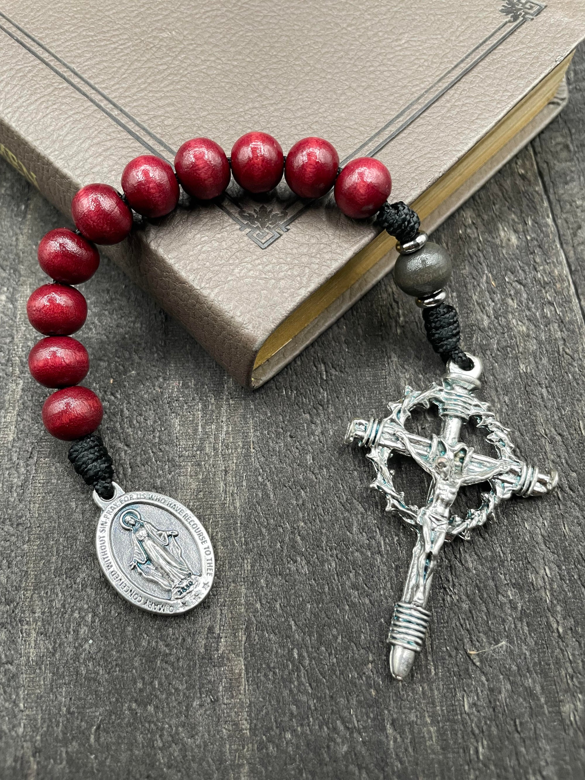 Close-up of a rosary with vibrant red beads, red knot accents, and a detailed silver crucifix featuring a thorny crown and a silver pendant of Mary, displayed on a book on a light surface, ideal for prayer and devotion.