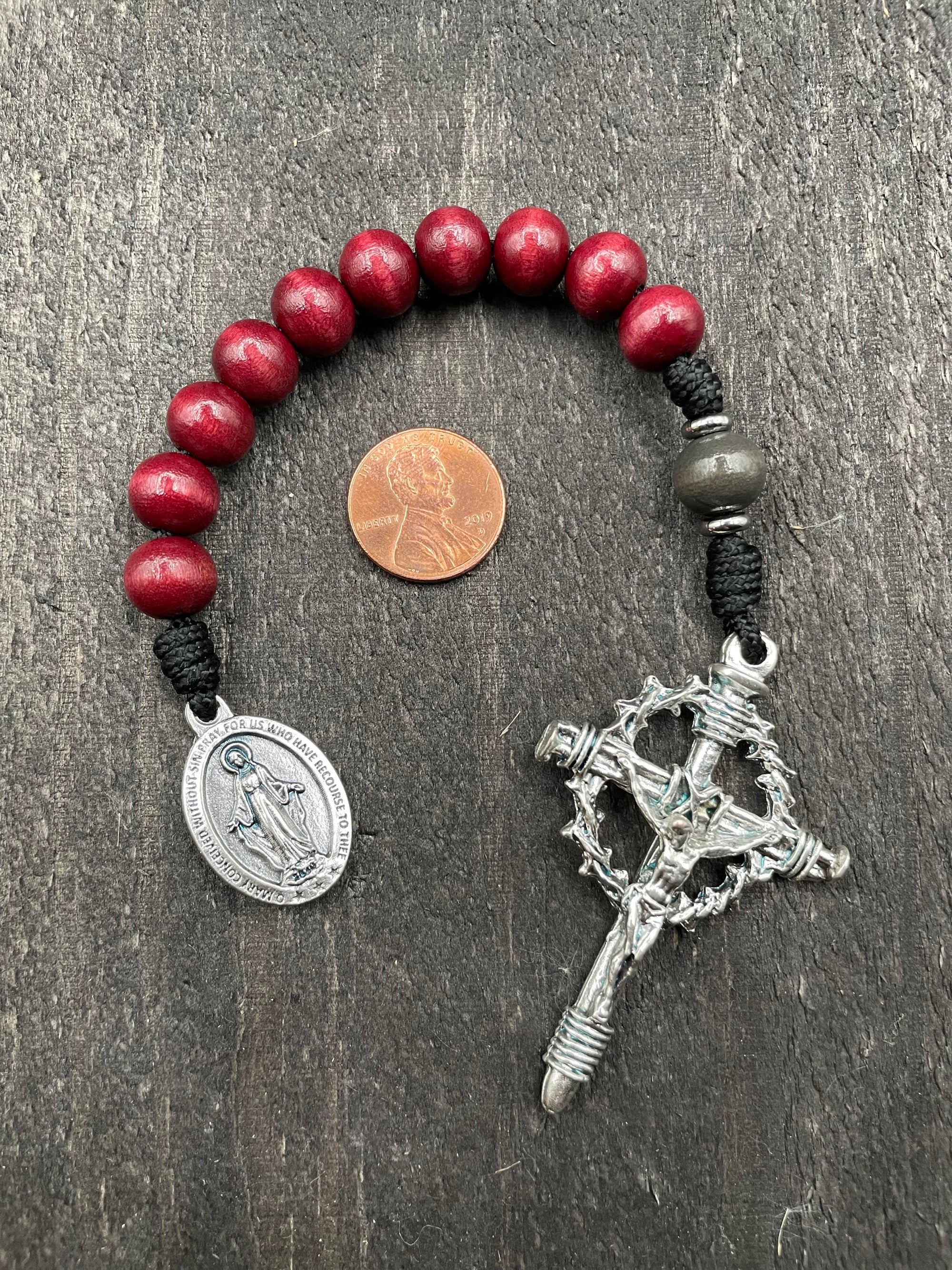 Close-up of a rosary with deep red beads, red knot accents, and an intricately designed crucifix pendant, ideal for prayer and spiritual reflection.