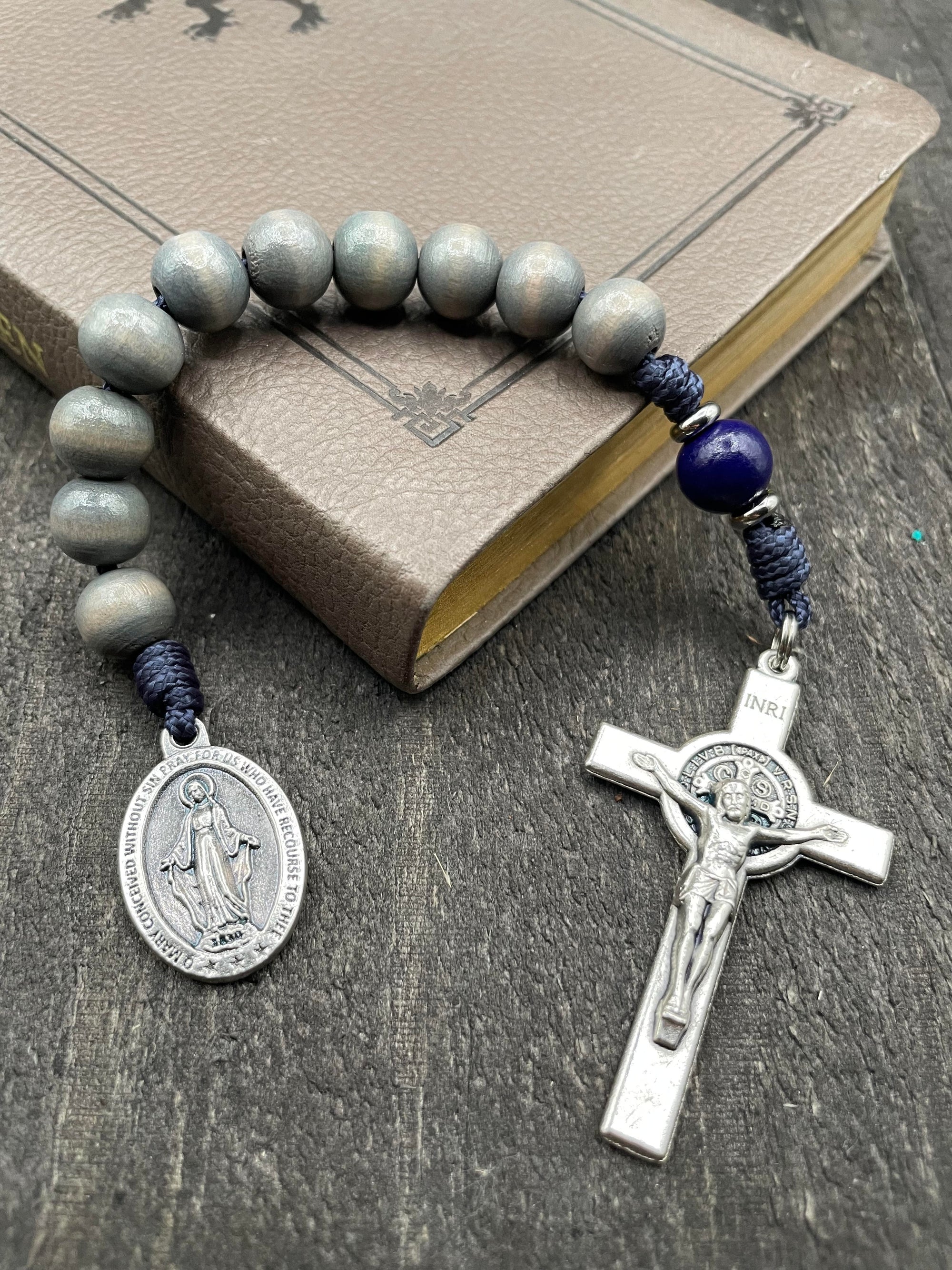Full view of a rosary with a detailed crucifix and pendant, gray beads, and strong knots, displayed on a book atop a gray wooden table, perfect for prayer and spiritual reflection.