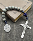 Full view of a rosary with a detailed crucifix and pendant, gray beads, and strong knots, displayed on a book atop a gray wooden table, perfect for prayer and spiritual reflection.