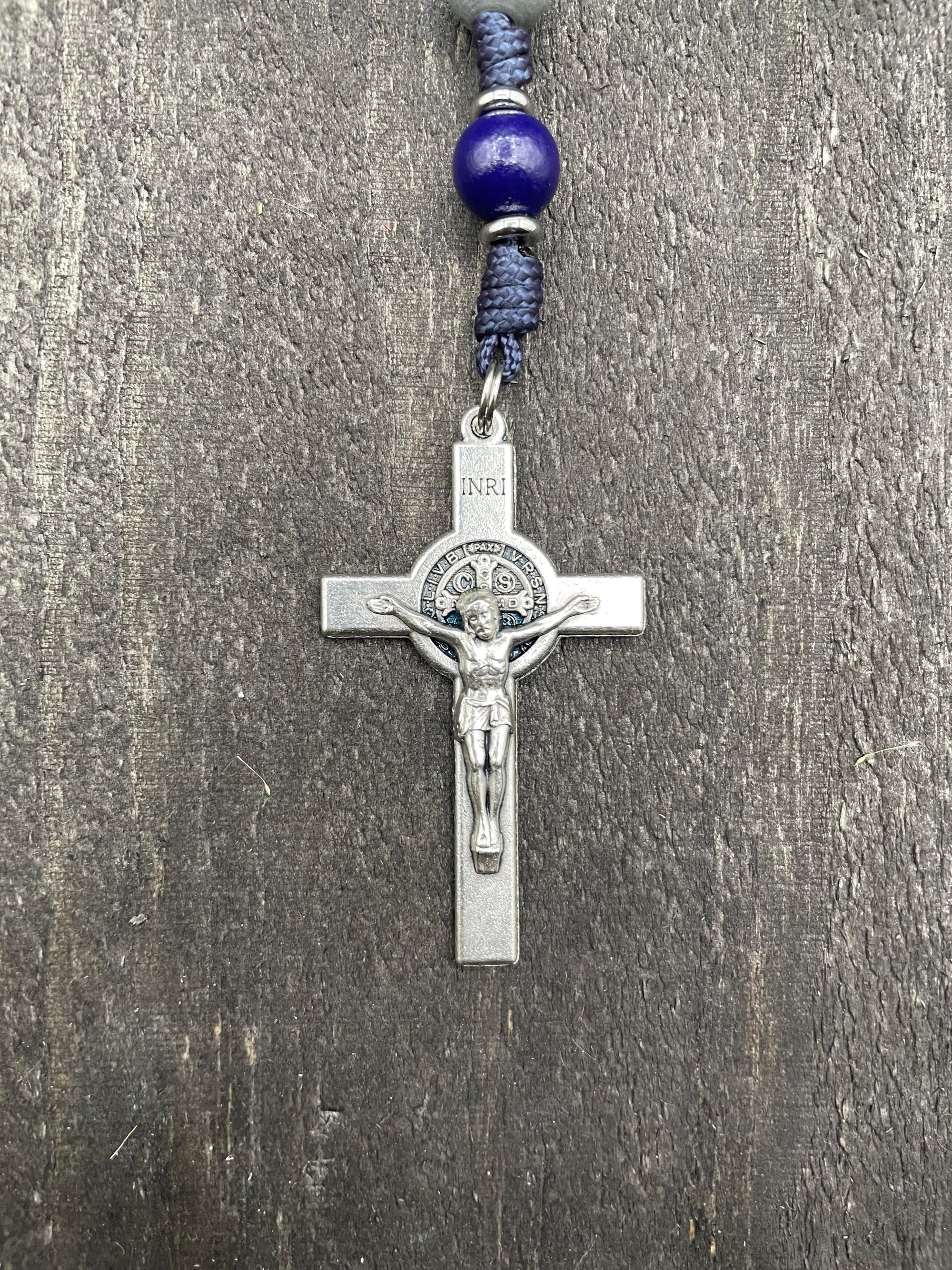 Close-up of a detailed crucifix with blue beads and durable knots, displayed on a light gray table, perfect for prayer and reflection.