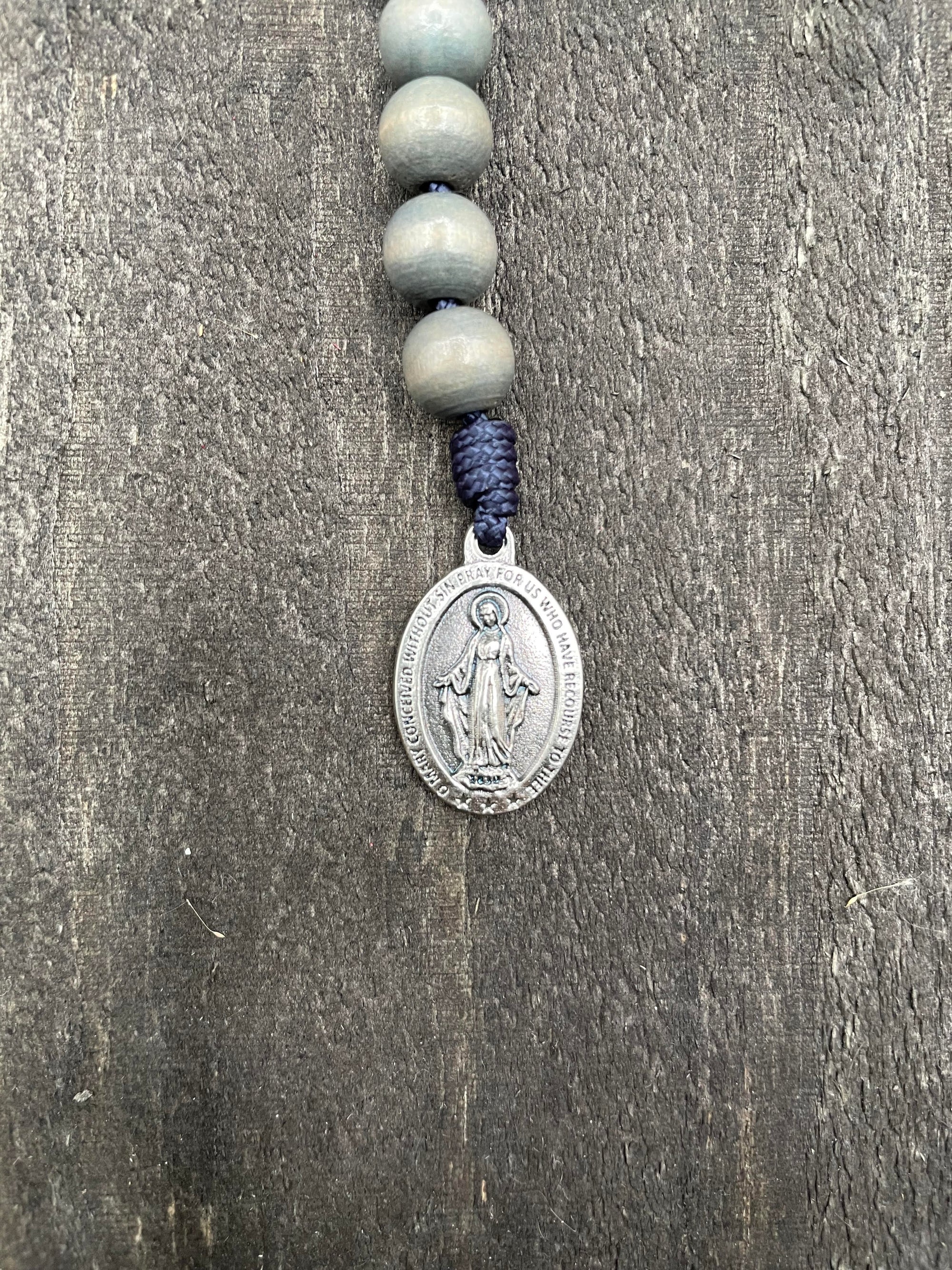Close-up of a detailed rosary pendant with gray beads and durable knots, displayed on a gray wooden table, ideal for prayer and reflection.