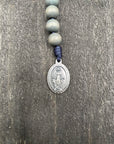 Close-up of a detailed rosary pendant with gray beads and durable knots, displayed on a gray wooden table, ideal for prayer and reflection.