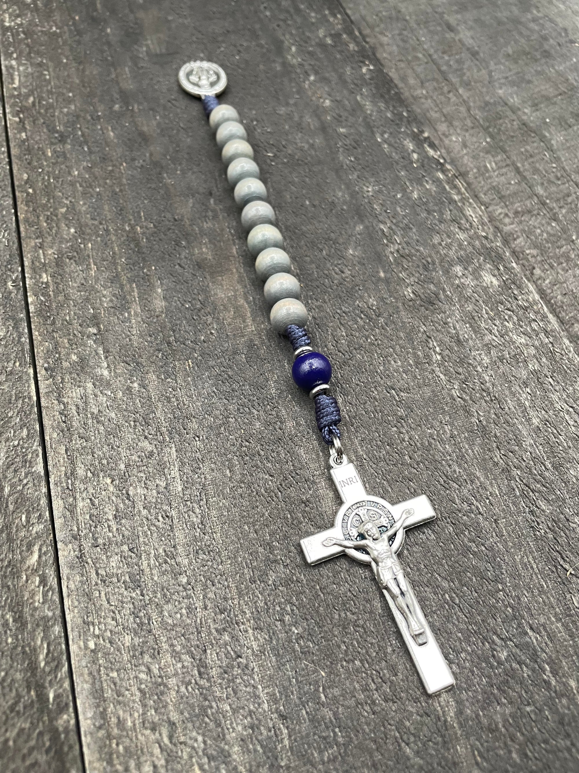 Close-up of a rosary with gray beads, durable knots, and a detailed silver crucifix with a pendant, displayed on a gray wooden table, perfect for prayer and devotion.
