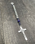 Close-up of a rosary with gray beads, durable knots, and a detailed silver crucifix with a pendant, displayed on a gray wooden table, perfect for prayer and devotion.