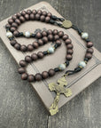 Wooden rosary with a metal crucifix resting on a closed brown book, placed on a dark wooden surface, ideal for prayer and spiritual reflection.