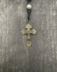A close-up of a metallic crucifix featuring a pearl bead, showcasing a durable knot on a wooden table.