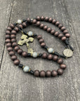 Close-up of a wooden rosary with intricately designed metal crucifix on dark textured background. This handcrafted prayer bead set features rich brown and gray beads, ideal for meditation and spiritual reflection.