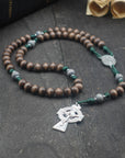 Handmade Celtic rosary featuring gray-brown wooden beads, silver crucifix, and emerald green paracord