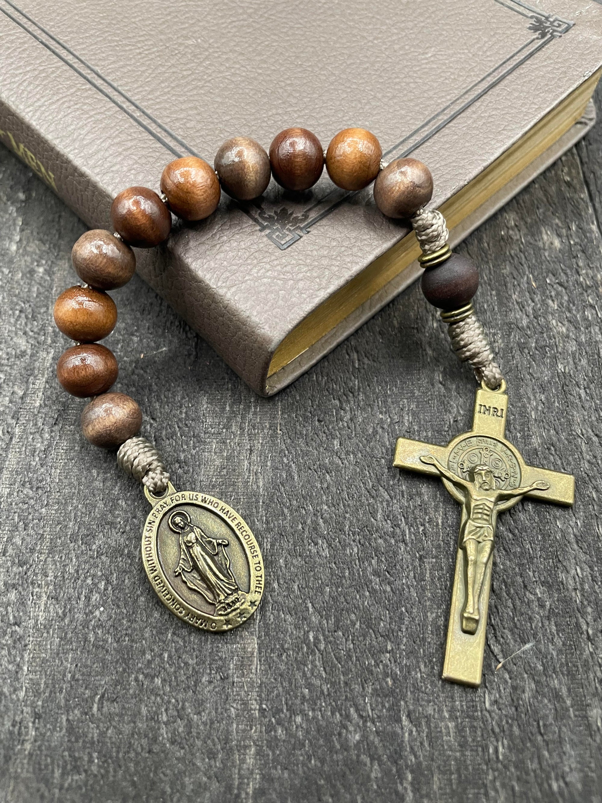 Full view of a rosary with sand-colored beads, durable knots, a detailed copper-colored crucifix, and a beautiful pendant, lying on a book placed on a light wooden table, ideal for prayer and spiritual reflection.