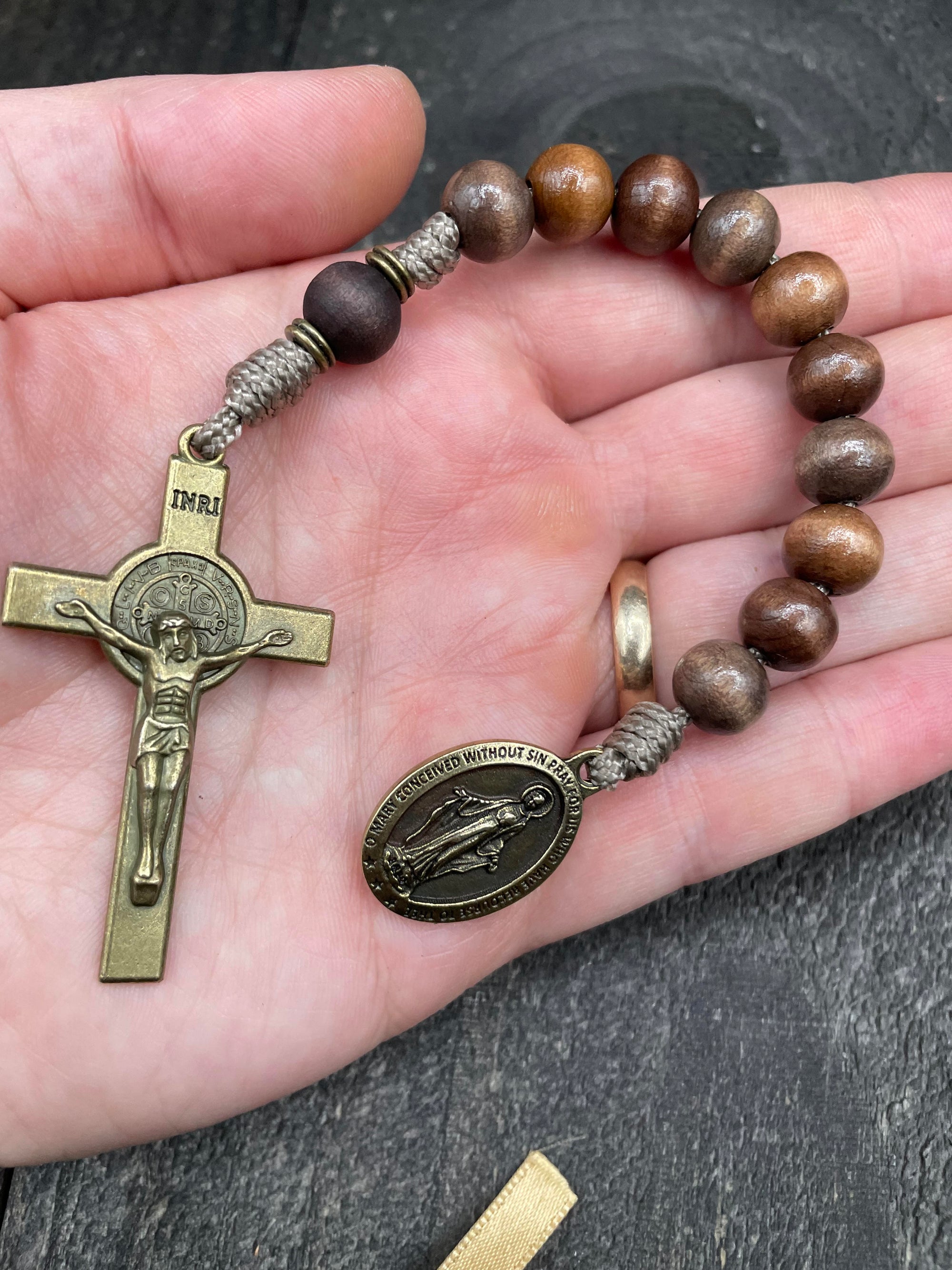 Full view of a rosary with sand-colored beads, durable knots, a detailed copper-colored crucifix, and a beautiful pendant, placed on a hand, ideal for prayer and spiritual devotion.