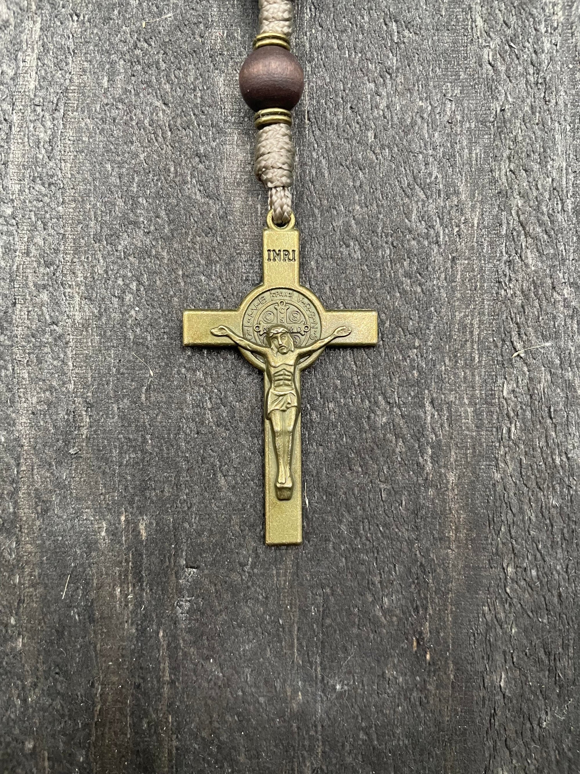 Close-up of a detailed copper-colored crucifix with sand-colored beads and durable knots, displayed on a light wooden surface, ideal for prayer and reflection.