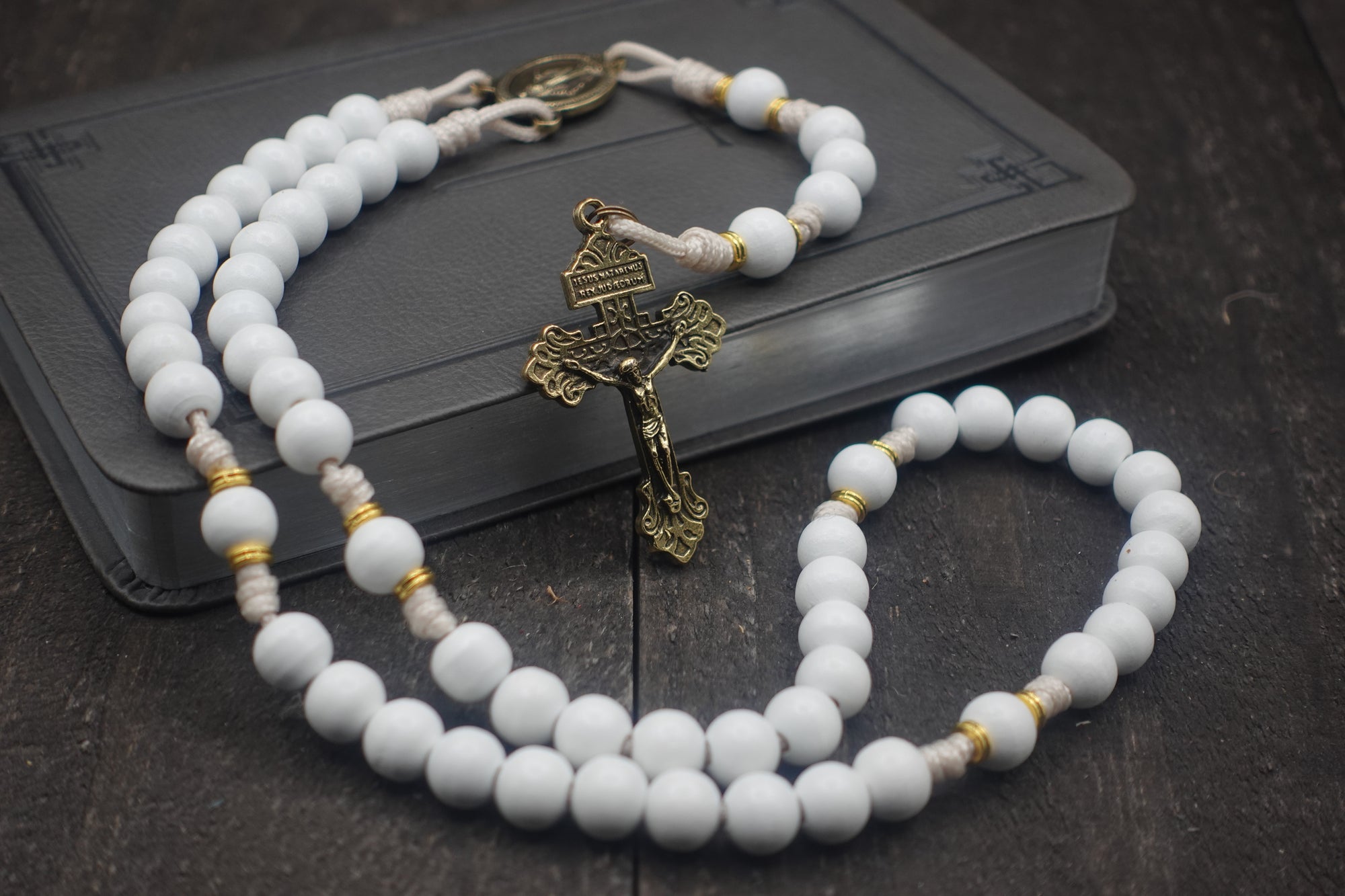 Heavenly Grace rosary with white wooden beads, gold spacers, bronze Pardon crucifix, and cream paracord