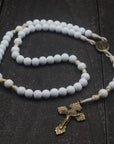 Handcrafted rosary featuring white wood beads, bronze crucifix, and gold spacer accents on cream paracord