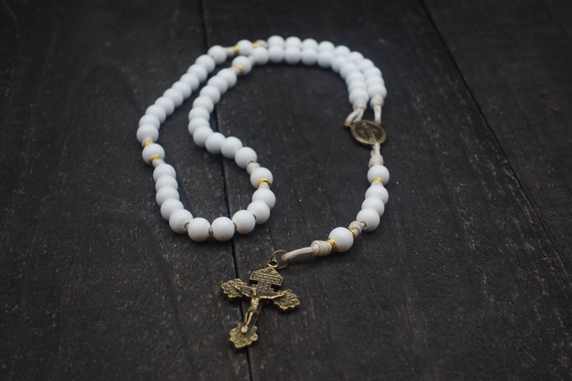 Handcrafted rosary featuring white wood beads, bronze crucifix, and gold spacer accents on cream paracord for weddings and first communion gifts