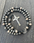 Durable black paracord rosary built for daily prayer with silver hardware and light gray wooden beads