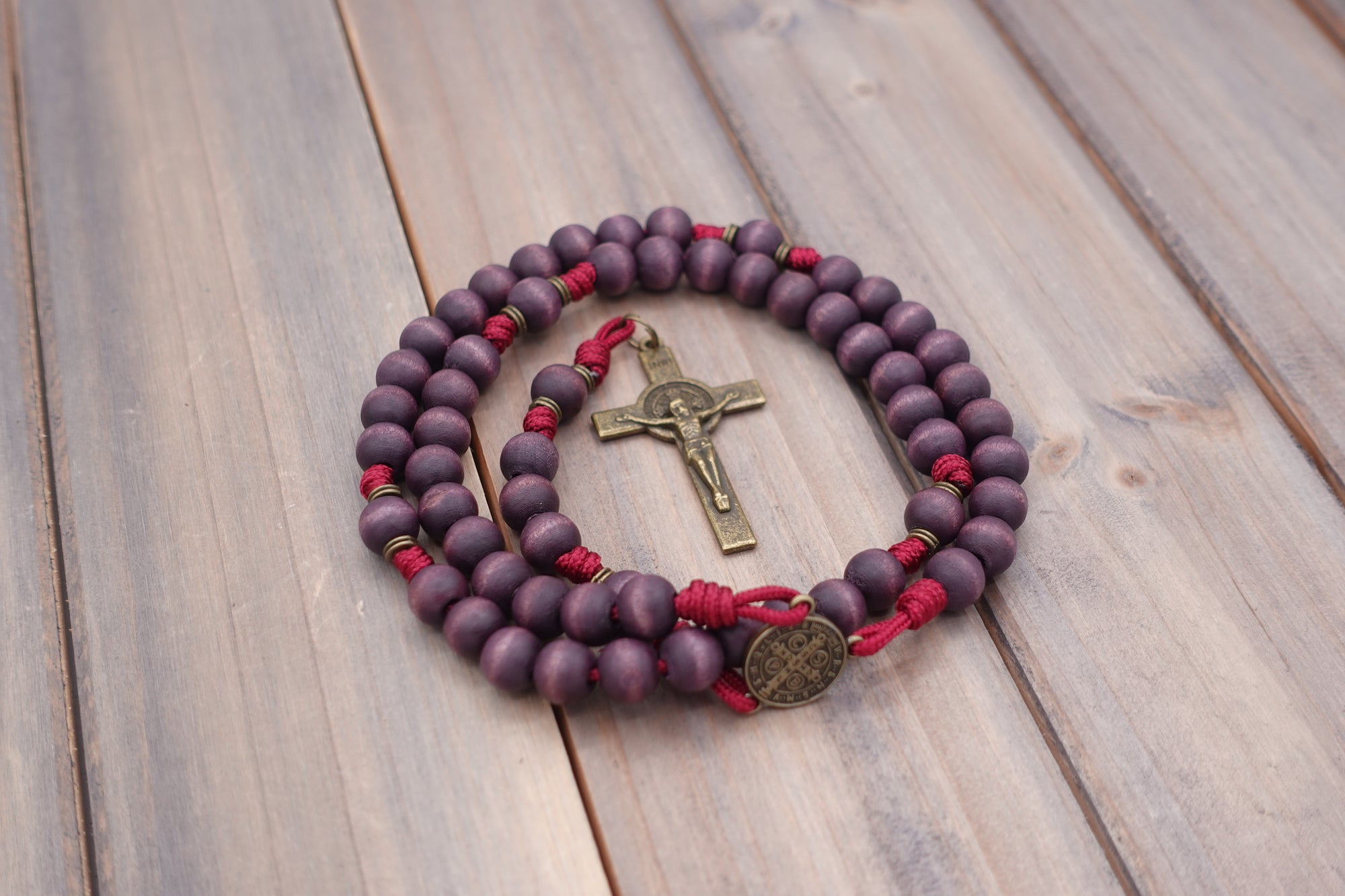 Handcrafted rosary featuring exclusive purple wood beads with bronze crucifix and St. Benedict medal centerpiece