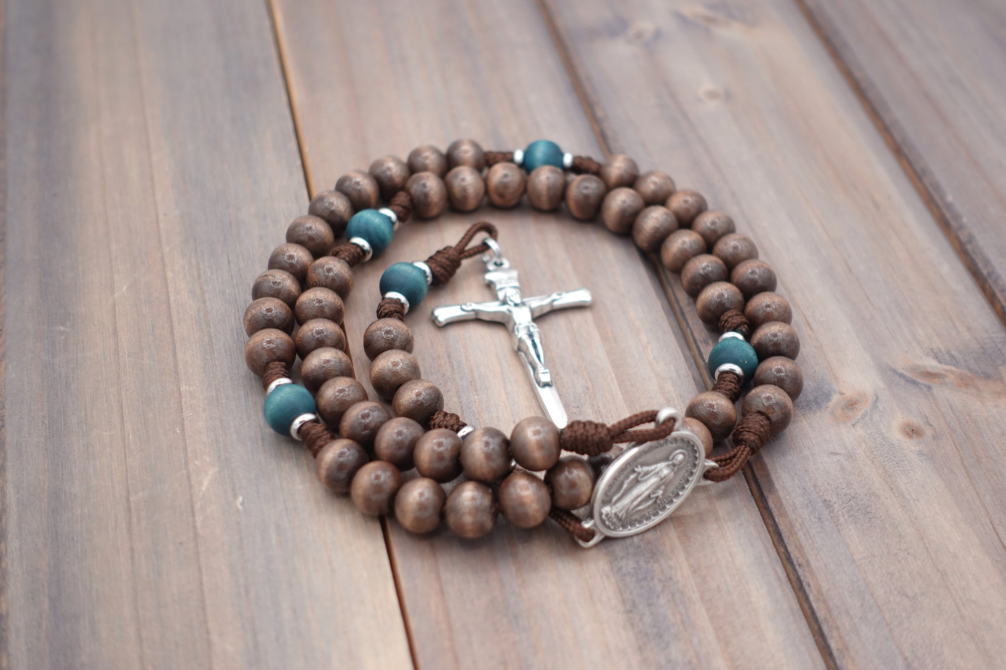 Close-up of silver Nails crucifix on St. Kateri rosary with gray-brown and teal wood beads