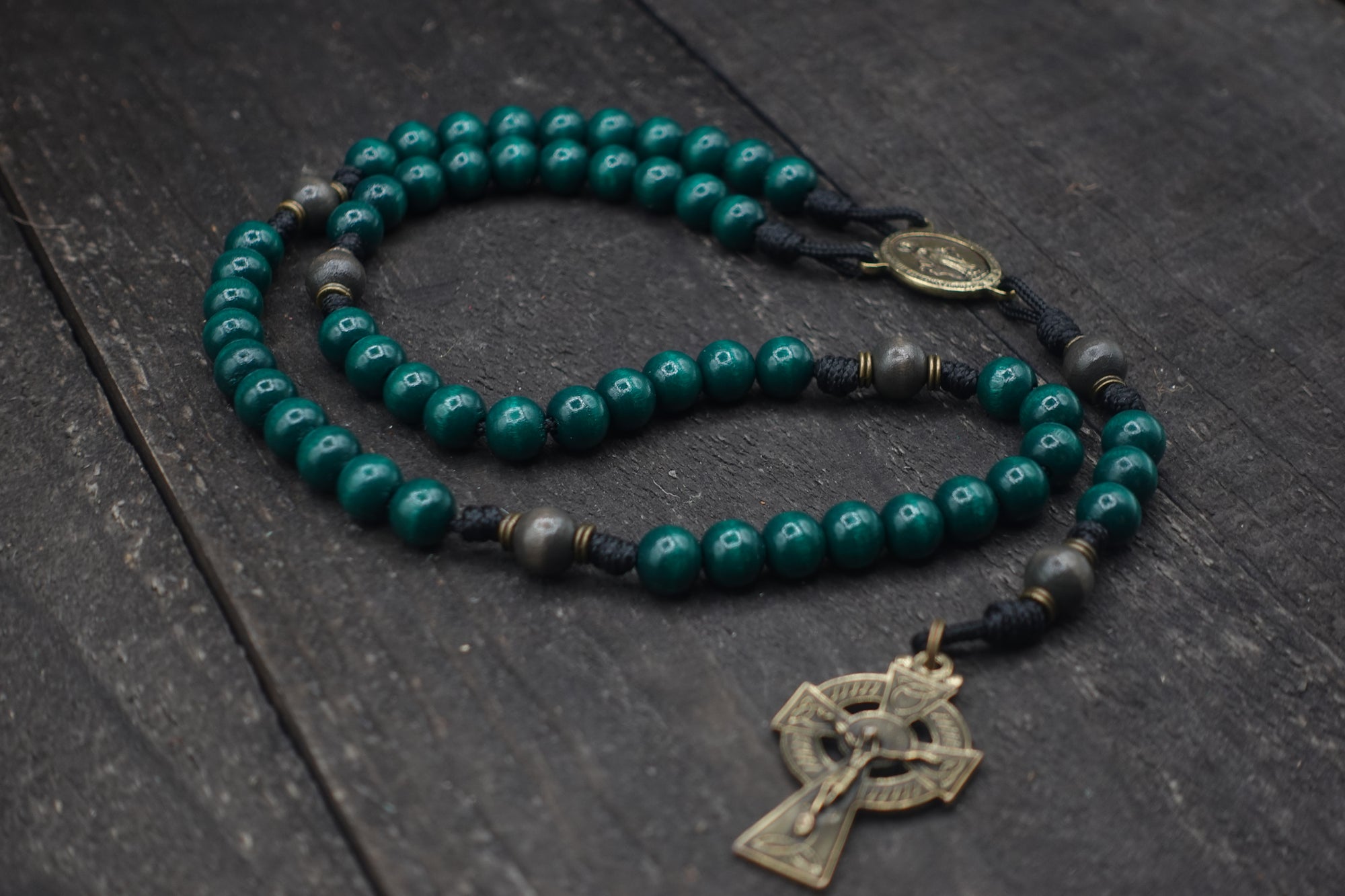 Durable black paracord rosary built for daily prayer with bronze Celtic hardware and green wooden beads