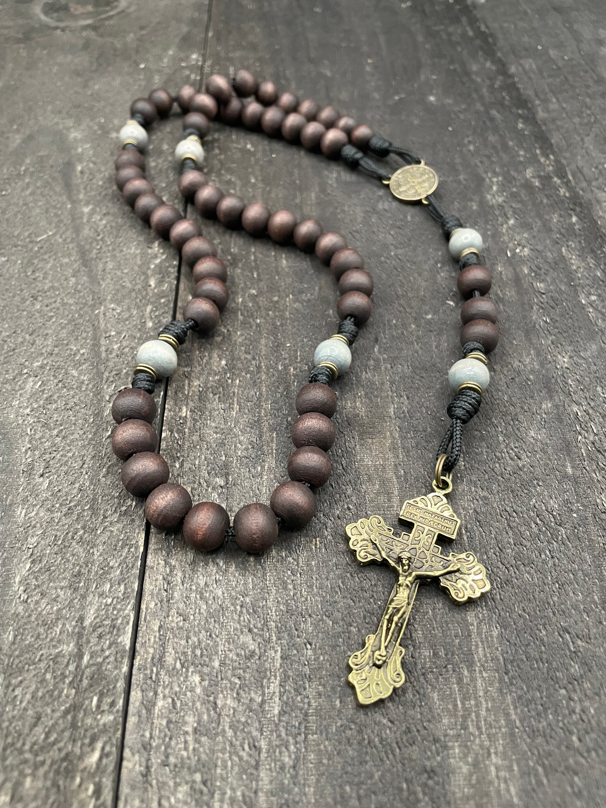 Wooden rosary with dark beads, a detailed crucifix, and a black string, displayed on a textured dark wood surface, creating a solemn and reflective tone.