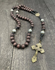 Wooden rosary with dark beads, a detailed crucifix, and a black string, displayed on a textured dark wood surface, creating a solemn and reflective tone.