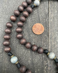 Close-up of a dark wooden bead rosary with a penny for size reference, displayed on a textured wooden surface, highlighting its craftsmanship and material quality.