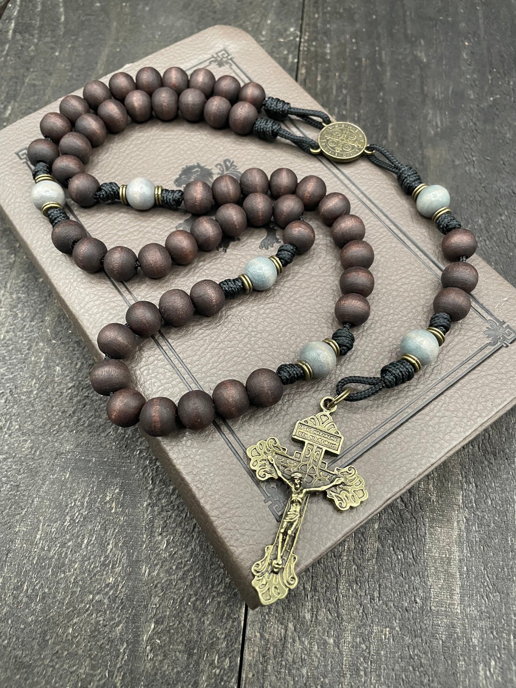 Wooden rosary with a metal crucifix resting on a closed brown book, placed on a dark wooden surface, ideal for prayer and spiritual reflection.