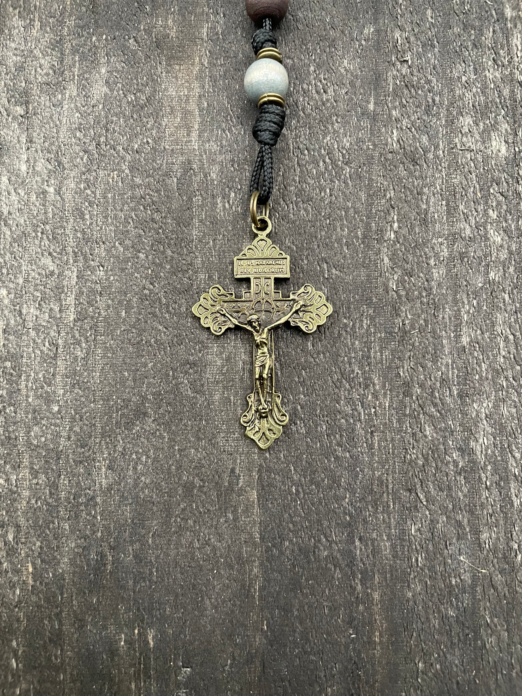A close-up of a metallic crucifix featuring a pearl bead, showcasing a durable knot on a wooden table.