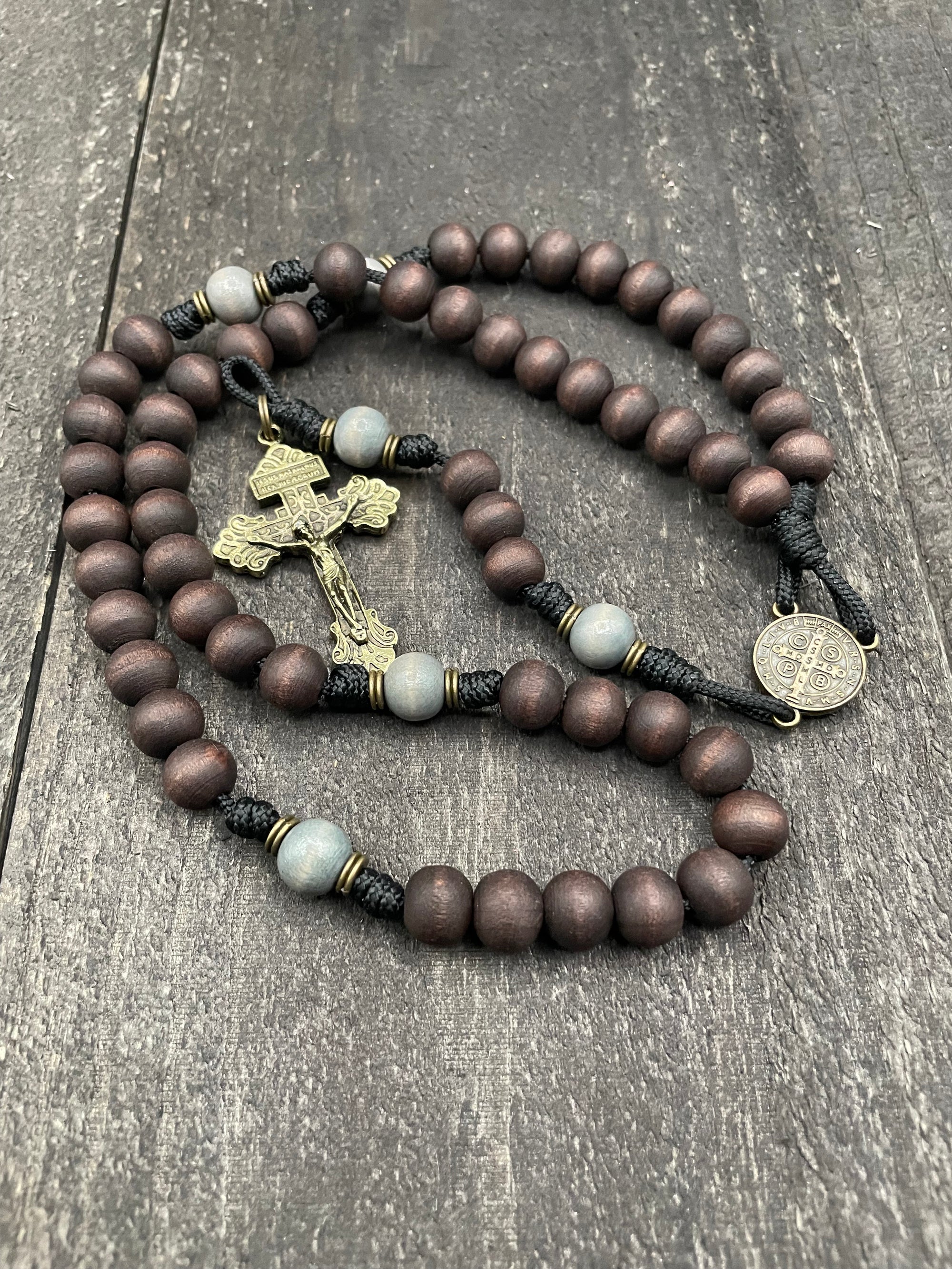 Close-up of a wooden rosary with intricately designed metal crucifix on dark textured background. This handcrafted prayer bead set features rich brown and gray beads, ideal for meditation and spiritual reflection.
