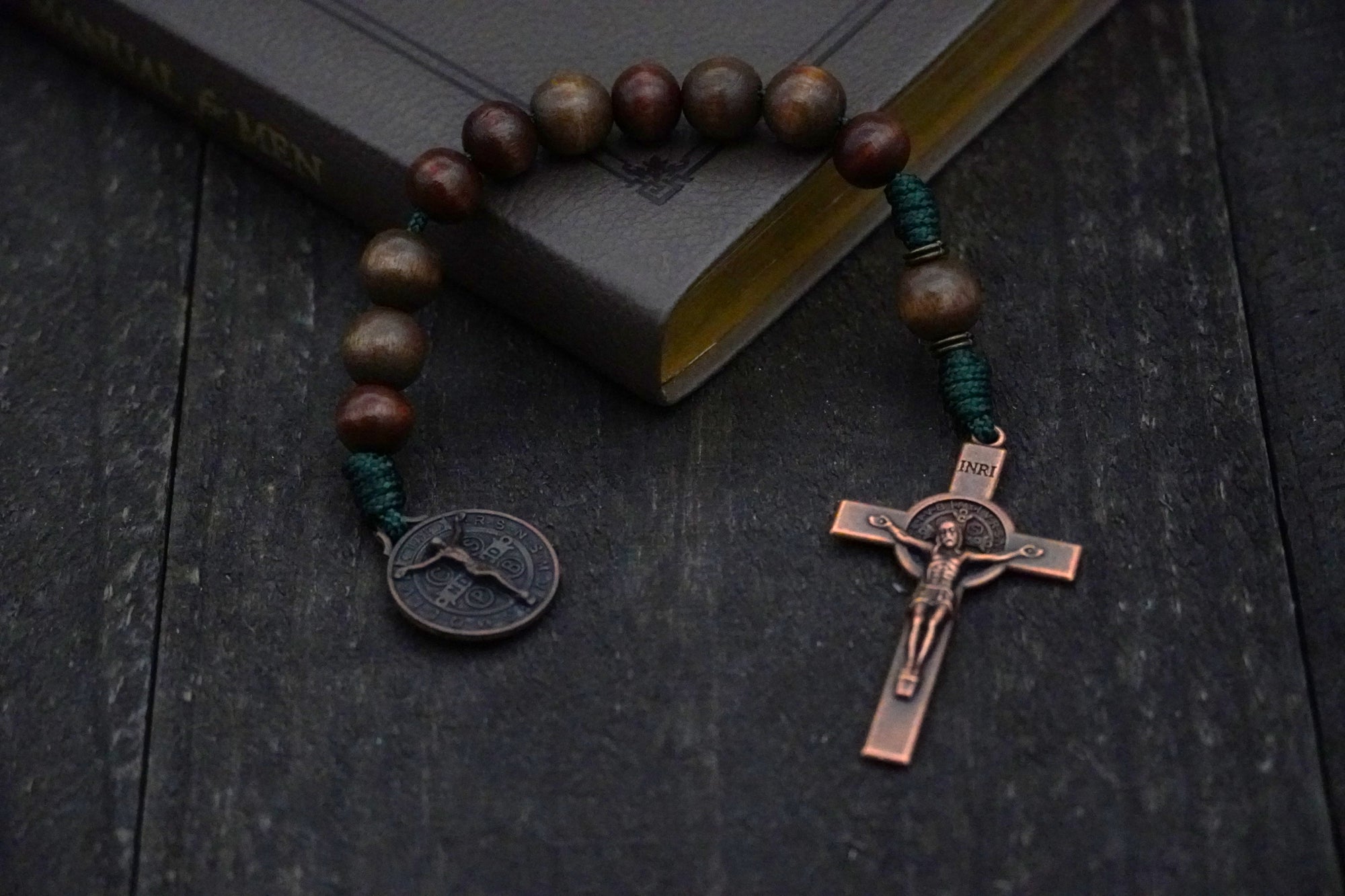 Pocket Woodsman rosary with gray-brown and dark brown wood beads, copper St. Benedict crucifix, and green paracord