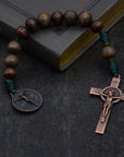 Pocket Woodsman rosary with gray-brown and dark brown wood beads, copper St. Benedict crucifix, and green paracord